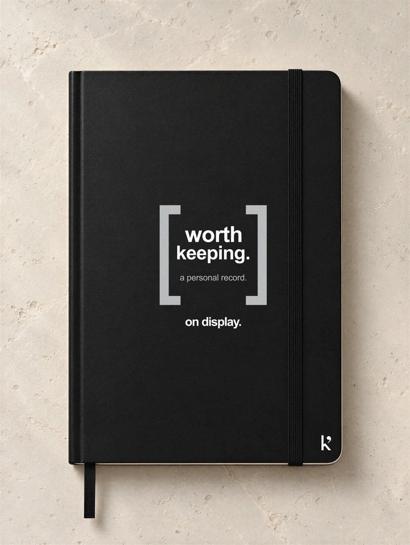 Black Karst notebook on pale stone, with centred worth keeping. cover lettering inside grey brackets and on display. below.